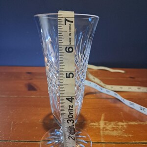 Puede incluir: Una copa de champ&aacute;n de cristal transparente con un patr&oacute;n de diamantes, que mide aproximadamente 18 cm de alto. La copa tiene una base redonda y una copa delgada y c&oacute;nica. Una cinta m&eacute;trica se coloca junto al vaso.