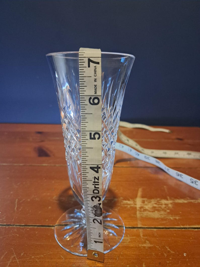 Puede incluir: Una copa de champ&aacute;n de cristal transparente con un patr&oacute;n de diamantes, que mide aproximadamente 18 cm de alto. La copa tiene una base redonda y una copa delgada y c&oacute;nica. Una cinta m&eacute;trica se coloca junto al vaso.