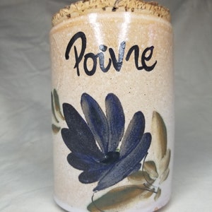 May include: A ceramic spice jar with a cork lid. The jar is decorated with a blue flower and green leaves. The jar is labeled "Poivre" which is French for pepper.