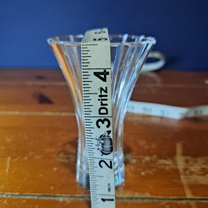 Puede incluir: Un jarr&oacute;n de vidrio transparente y acanalado con la parte superior acampanada. Una cinta m&eacute;trica muestra que el jarr&oacute;n mide aproximadamente 10 cm de alto. El jarr&oacute;n est&aacute; sobre una superficie de madera con un fondo azul oscuro.