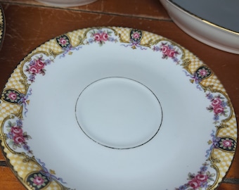 May include: A white saucer with a gold rim and a floral pattern in shades of pink, blue, and black. The saucer has a smaller, white saucer in the center.