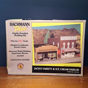 May include: A Bachmann Plus model building kit for Jack's Variety & Ice Cream Parlor. The box shows a detailed image of the model, with text indicating a precise HO scale and authentic period colours. The kit includes instructions.