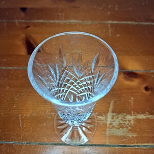 Puede incluir: Una copa de champ&aacute;n transparente, tallada en cristal, con un patr&oacute;n detallado en el cuenco y una base redonda. El vaso est&aacute; colocado sobre una superficie de madera, mostrando su intrincado dise&ntilde;o y forma elegante. El vaso mide unos 18 cm de alto.