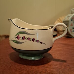 May include: A white creamer with a blue and green base and a floral design featuring pink flowers and green leaves.