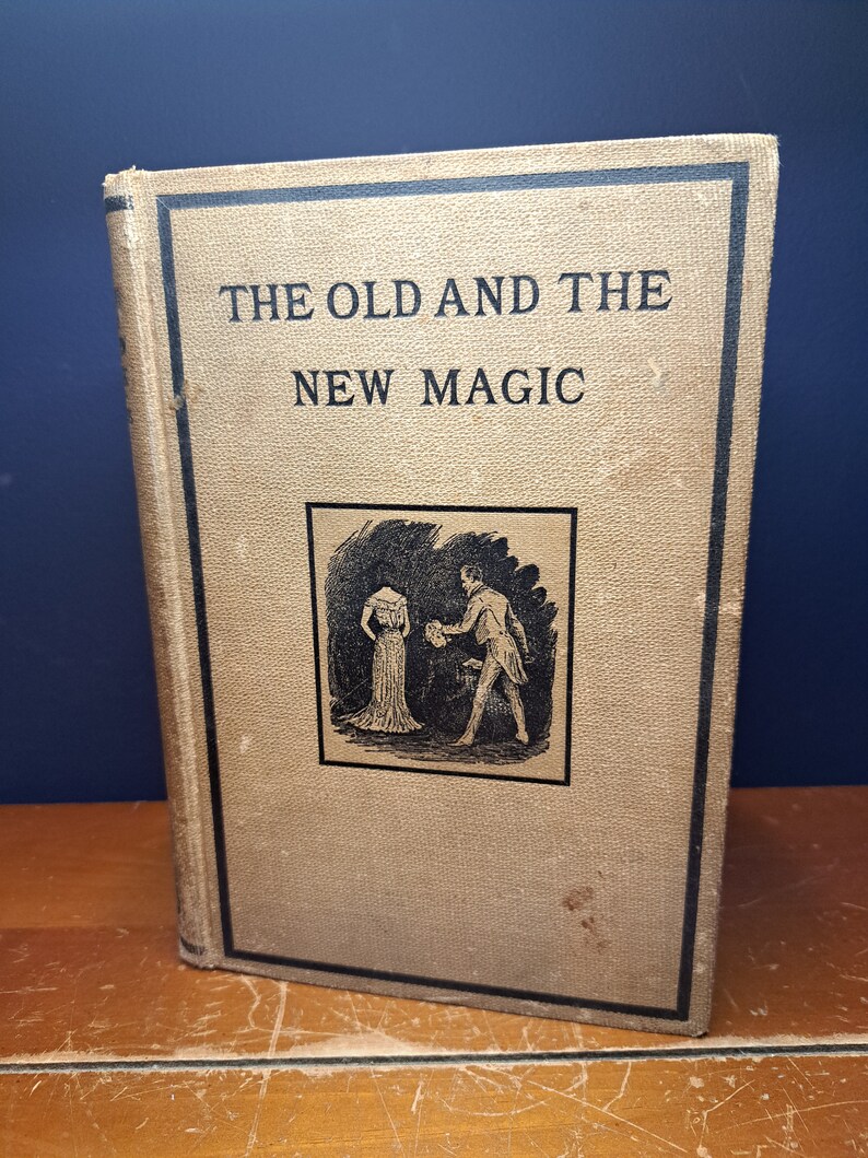Może przedstawiać: Antyczna książka z beżową okładką i czarnym tekstem, kt&oacute;ry brzmi "The Old and The New Magic". Okładka zawiera czarno-białą ilustrację mężczyzny i kobiety w strojach z epoki.