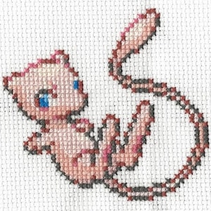 May include: Cross-stitch embroidery of a pink and gray Pokemon character, known as Mew, with a blue eye. The character is curled up in a circle.