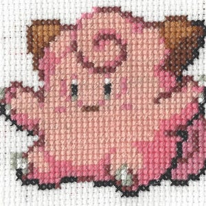 Könnte beinhalten: Rosa und braune Kreuzstich-Stickerei eines Pokemon-Charakters mit einem eingerollten Schwanz und braunen Ohren.