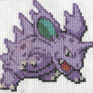 Puede incluir: Punto de cruz morado y verde de un personaje de Pokemon. El personaje es una criatura morada con un ojo verde y una boca roja.