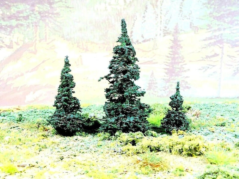 May include: Three green pine trees against a blurred background of a light blue and yellow sky. The trees are different sizes and shapes, with the tallest tree in the center.