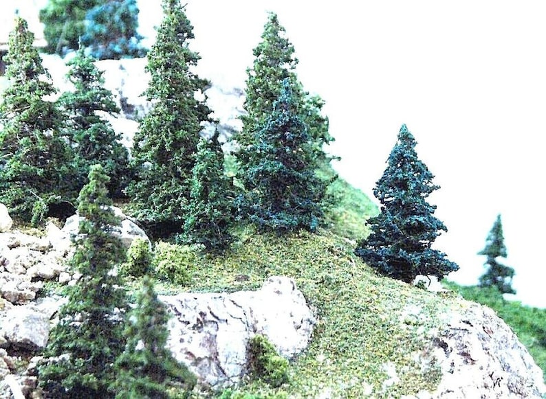 May include: A close-up of a miniature model train landscape with several green pine trees and a rocky hillside.