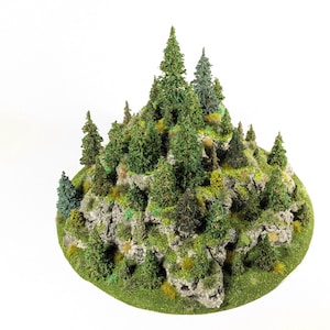 May include: A miniature model of a forested mountain. The base is a circular shape covered in green grass. The mountain is rocky with various shades of green trees and shrubs. The trees are of different sizes and types, creating a realistic landscape.