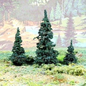May include: Three miniature evergreen trees with dark green foliage, set against a painted backdrop of a forest scene.