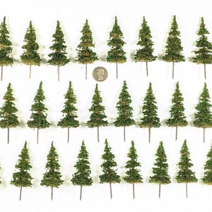 May include: A collection of miniature green model trees with brown stems, arranged in rows on a white background. The trees are detailed with textured foliage, and a coin is placed among them for scale. Ideal for model train sets or dioramas.