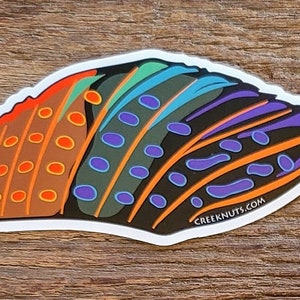 May include: A colorful sticker with a stylized design of a butterfly wing. The wing is made up of multiple sections, each with a different color and pattern. The colors include orange, red, green, blue, purple, and black. The sticker has a white border and the text "CREEKNUTS.COM" is printed on the bottom right corner.