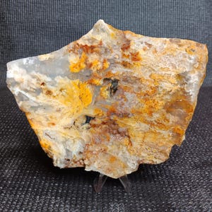 Puede incluir: Una losa de ágata grande e irregular con un esquema de color blanco, gris y naranja. La ágata tiene un aspecto estratificado y bandeado con una variedad de texturas.