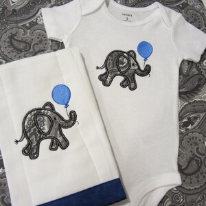 May include: A white baby onesie and a white burp cloth with a blue and gray paisley elephant holding a blue balloon embroidered on each. The onesie has the text "carter's" and the number "3" on the tag.