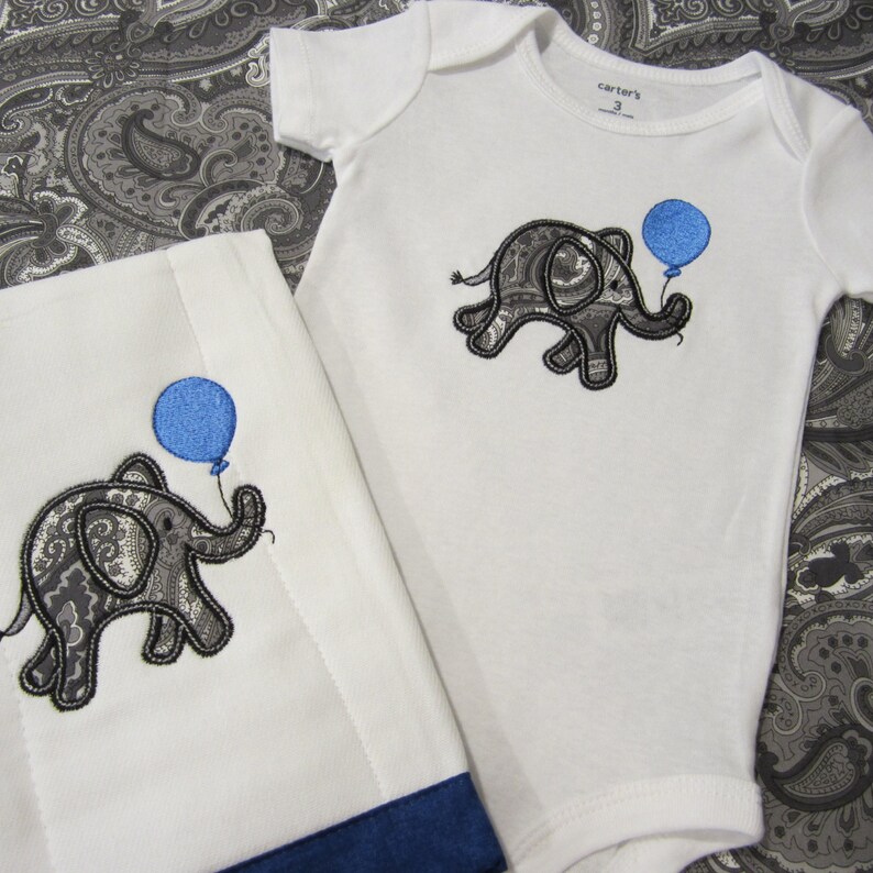 May include: A white baby onesie and a white burp cloth with a blue and gray paisley elephant holding a blue balloon embroidered on each. The onesie has the text "Carter's" on the tag.