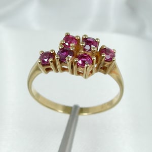 May include: A gold ring with a cluster of pink ruby stones set in a delicate, intricate design.