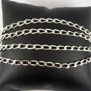 May include: Four silver curb chains of different lengths on a black velvet background.