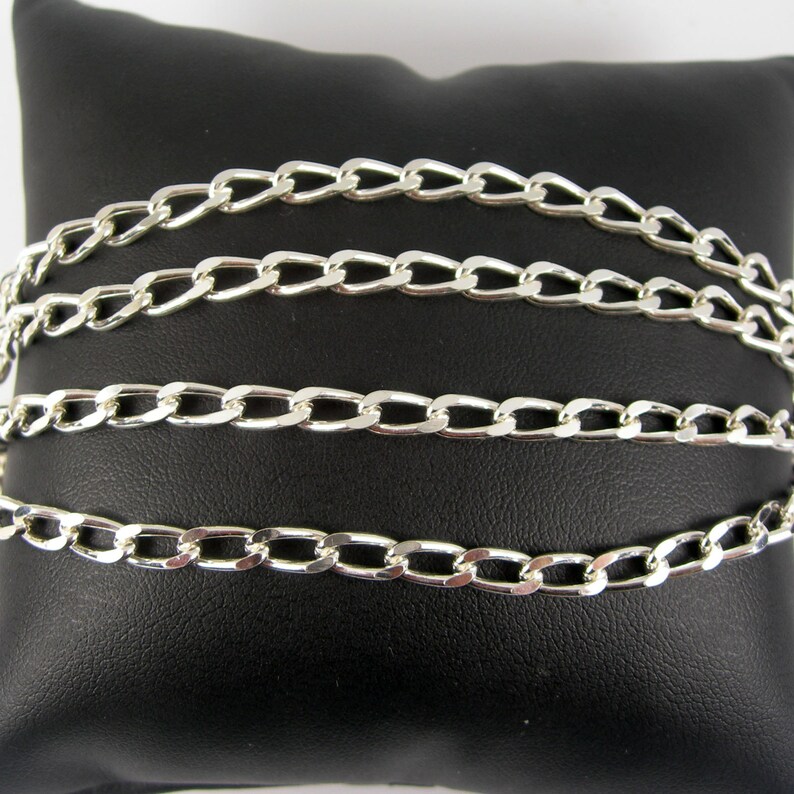 May include: Four silver curb chains of different lengths on a black velvet background.