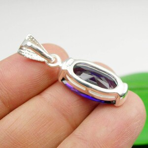 May include: A silver pendant featuring a purple gemstone set within a detailed silver frame. The pendant is displayed on a hand.