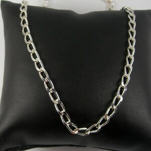 May include: A silver chain necklace with a curb link design. The chain is displayed on a black velvet pillow.