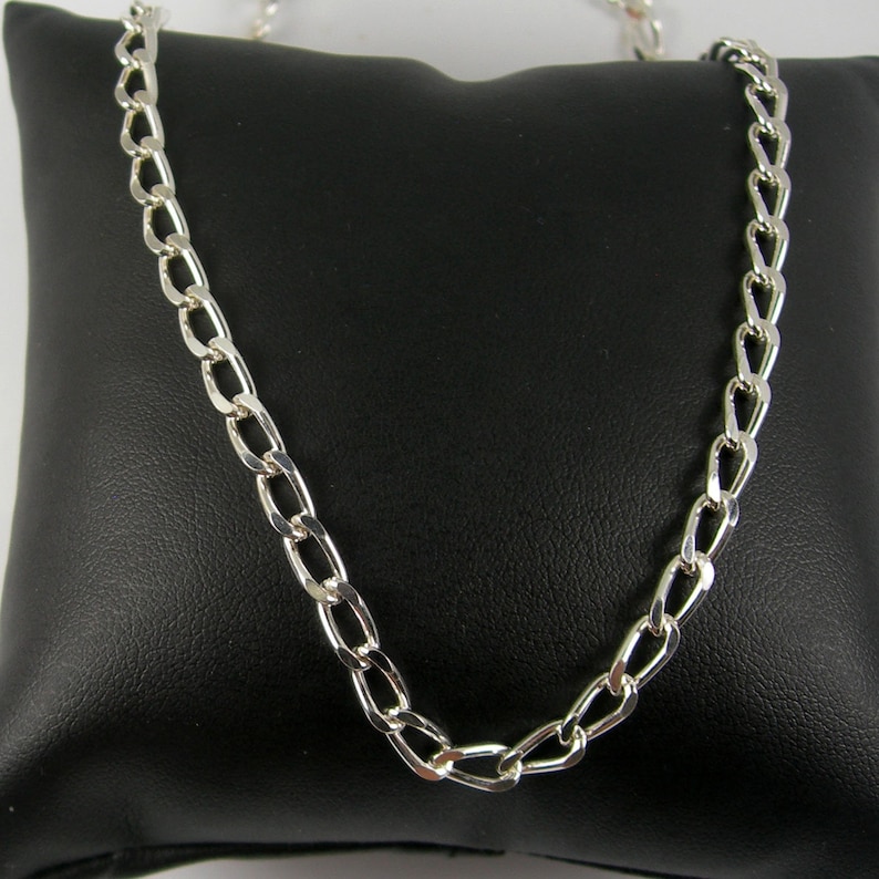 May include: A silver chain necklace with a curb link design. The chain is displayed on a black velvet pillow.