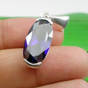 May include: A silver pendant featuring a large, faceted, oval-shaped purple gemstone.