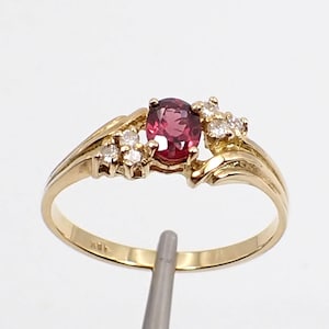 May include: A gold ring with a red gemstone and small white gemstones. The ring is set in a delicate, swirling design.