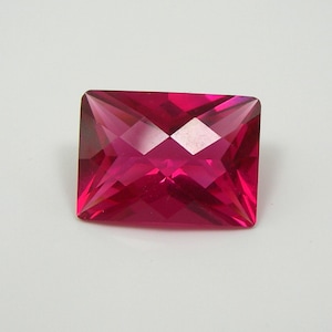 Könnte beinhalten: Ein lebendiger, tiefrosa, quadratischer Edelstein mit facettiertem Schliff. Der Edelstein ist vor einem weißen Hintergrund platziert.