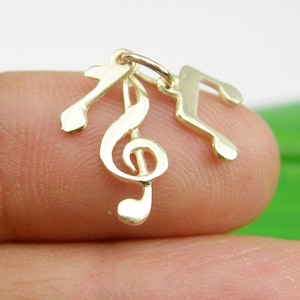 Puede incluir: Encanto de oro con tres notas musicales, incluyendo una clave de sol y dos corcheas.