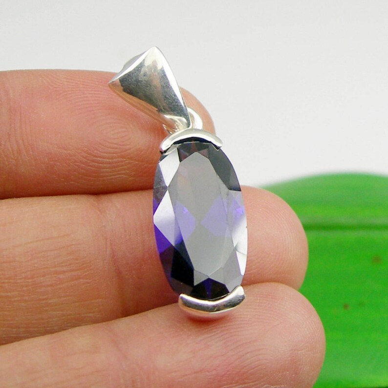 May include: A silver pendant featuring a large, faceted, oval-shaped purple gemstone.