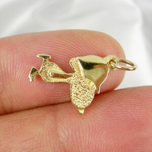May include: A small, gold-colored charm in the shape of a saddle. The charm has a textured surface and a loop for attaching to a necklace or bracelet. The saddle has a detailed design, including the seat, stirrups, and horn.