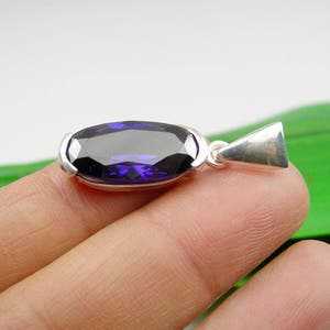 May include: A silver pendant featuring a large, oval-shaped, dark purple gemstone.