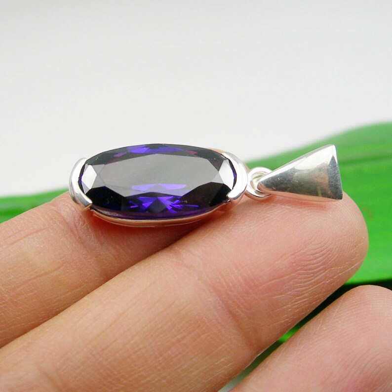 May include: A silver pendant featuring a large, oval-shaped, dark purple gemstone.