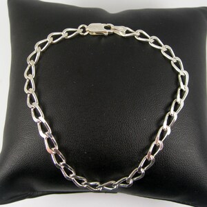 May include: A silver chain bracelet with a lobster clasp closure. The chain is made of a flat, oval-shaped link.