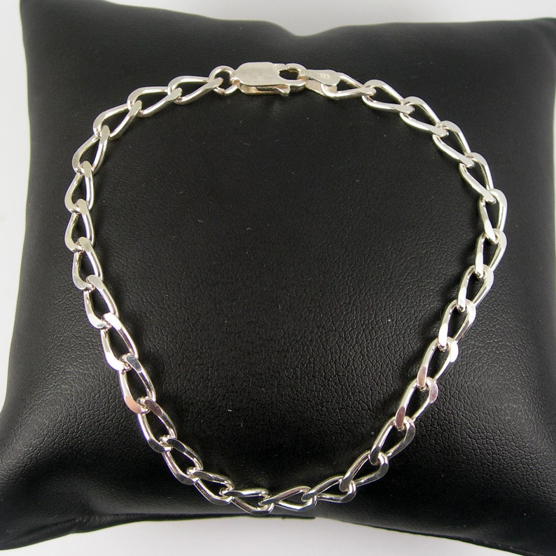 May include: A silver chain bracelet with a lobster clasp closure. The chain is made of a flat, oval-shaped link.