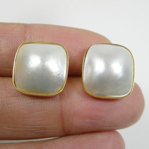 May include: A pair of white pearl earrings with gold settings. The pearls are square shaped and have a smooth, glossy finish.