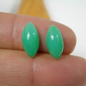 May include: Two green marquise-shaped gemstones, likely chrysoprase, are shown on a finger.