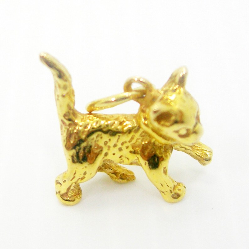 K&ouml;nnte beinhalten: Ein goldfarbener Anh&auml;nger in Form eines laufenden K&auml;tzchens. Der Anh&auml;nger hat oben eine Schlaufe zum Anbringen an einer Halskette oder einem Armband.