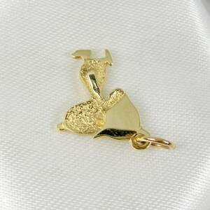 May include: A gold-colored pendant in the shape of a calla lily. The pendant has a textured surface on the back and a smooth, polished finish on the front. A small loop is attached for hanging.