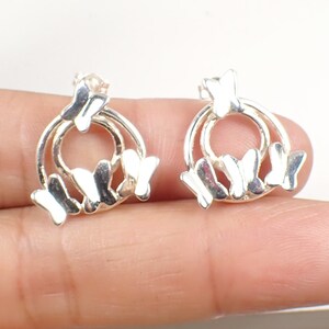 Könnte beinhalten: Silberne Schmetterlings-Ohrringe mit einem Kreisdesign. Die Ohrringe zeigen mehrere Schmetterlinge, die in einem Kreis angeordnet sind.