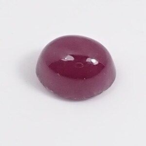 Pode incluir: Uma gema cabochão vermelho-escuro com uma superfície lisa e polida.