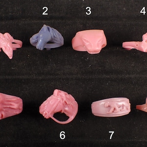 May include: Eight different pink and purple plastic rings with various animal and geometric designs. The rings are numbered 1 through 8.