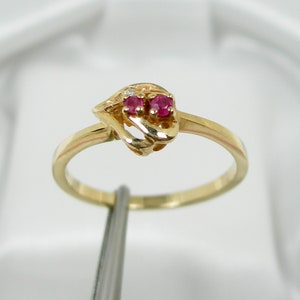 Op de afbeelding: Een gouden ring met een delicaat ontwerp met twee rode edelstenen en een kleinere witte edelsteen.