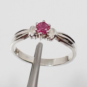 May include: A silver ring with a pink gemstone set in the center. The ring has a simple, elegant design.