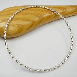 May include: A silver twisted bangle bracelet. The bracelet is made of a single piece of wire that has been twisted into a spiral shape.