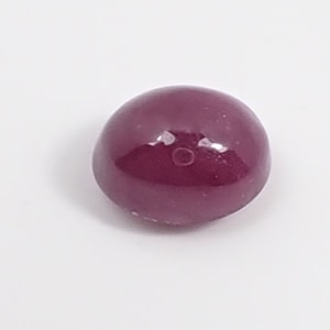 May include: A deep red cabochon gemstone with a smooth, polished surface.
