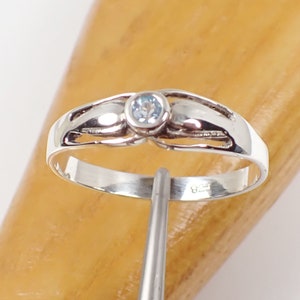 May include: A silver ring with a light blue gemstone set in the center. The ring has a delicate, intricate design.