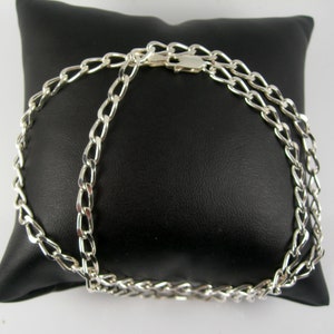 May include: A silver chain necklace with a curb link design. The chain is on a black velvet pillow.